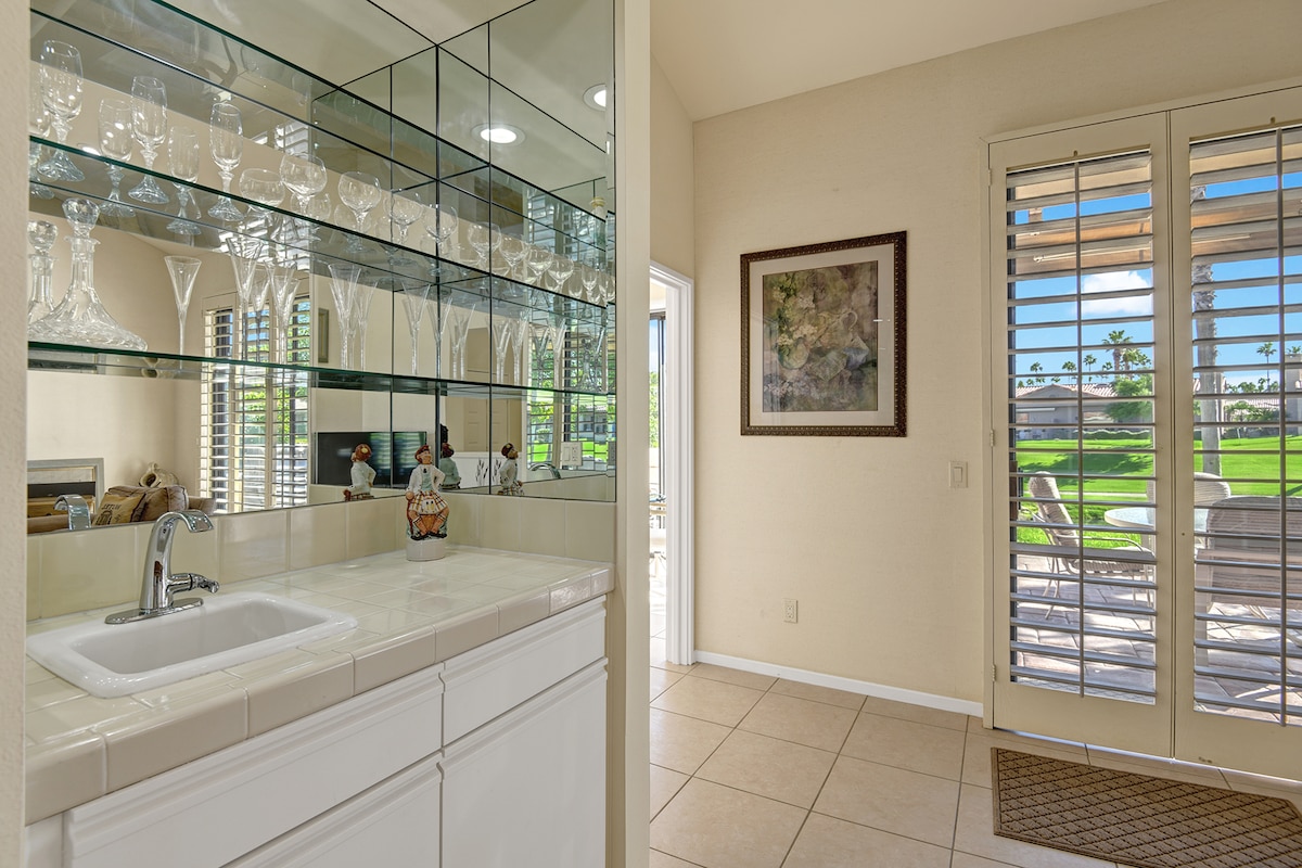 Clean, elegant wet bar with glass shelving and a view overlooking the lush green golf course—perfect for entertaining while you enjoy your vacation.