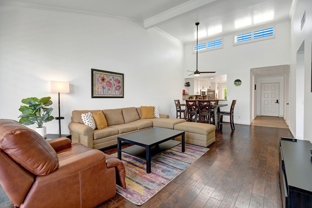 Step into your spacious living area where high ceilings and warm wood floors create an inviting atmosphere. Relax on the plush sectional or settle into the leather chair, enjoying the natural light that fills this open, airy space.