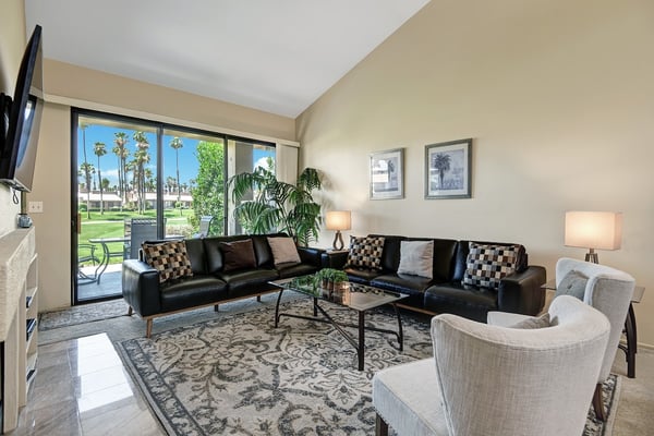 Stretch out on plush leather seating in your sunlit living room, where floor-to-ceiling windows frame a peaceful view of palm trees and lush greens beyond your private patio.