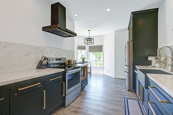 Sleek modern kitchen with elegant cabinetry, golden hardware accents, and generous countertops. Natural light floods through windows overlooking greenery, creating a bright and inviting culinary space.