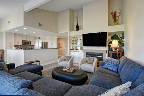 Spacious living room with vaulted ceilings and soft natural light. Plush seating, fireplace, and open sightlines to the modern kitchen create the perfect retreat.