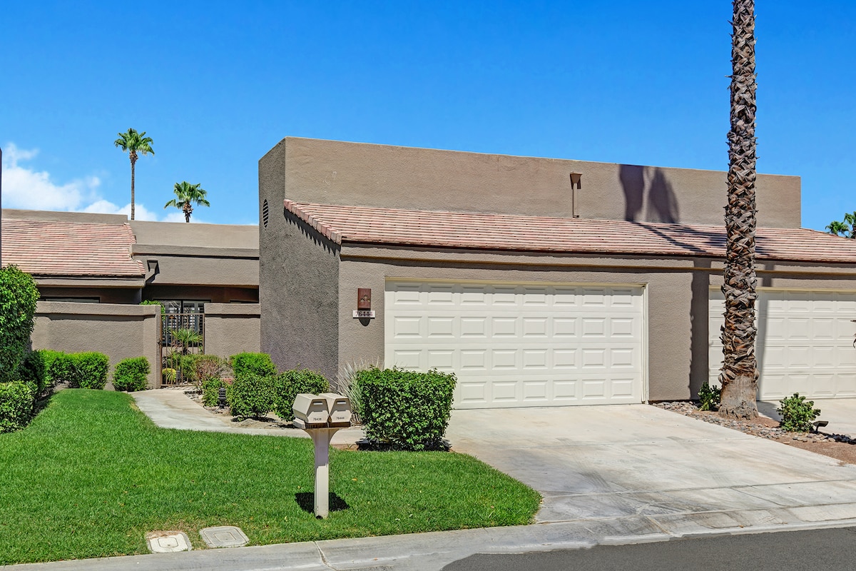 A contemporary vacation rental with a tidy lawn, palm trees, and a two-car garage set beneath bright desert skies—a warm and welcoming retreat awaits.