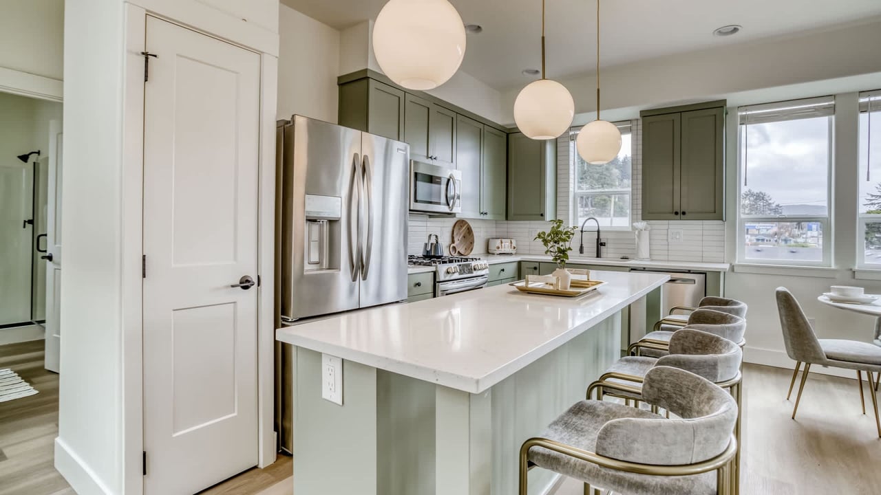 Picture yourself whipping up your favorite dishes in this beautifully appointed kitchen. Sage green cabinetry, bright white counters, stainless appliances, and cozy seating make this a space where you'll love to cook and gather.