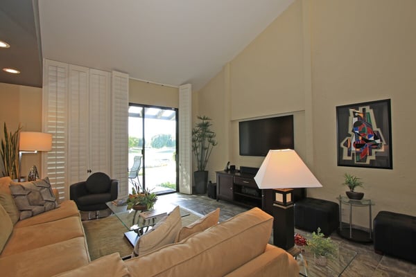 Relax in your spacious living room with vaulted ceilings and plush seating arranged for conversation and comfort. Natural light pours through glass doors, connecting you to the outdoor view beyond.
