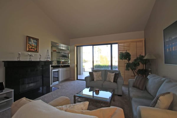Sink into plush sofas and enjoy your favorite shows or unwind by the fireplace in this inviting living room, with sunny views and touches of greenery throughout.