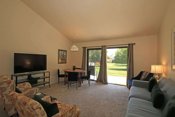 Step into your bright living area where natural light floods through glass doors opening to peaceful green lawns. Relax on comfy seating, gather at the dining table, or unwind with your favorite shows in this open, welcoming space.