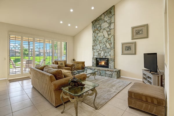 Unwind in your inviting living room featuring a stunning stone fireplace, vaulted ceilings, and elegant furnishings. Through the plantation shutters, glimpse the green lawn awaiting your morning coffee.