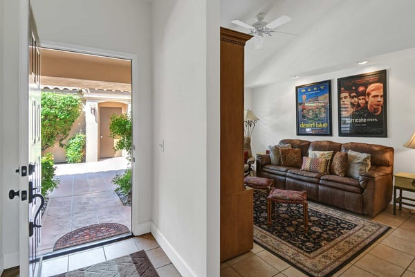 Step through the entryway into your inviting living room, where a plush leather sofa beckons you to relax. Bright natural light welcomes you through the open door, while the ceiling fan keeps the air refreshingly cool.