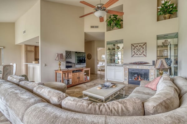Sink into plush seating and unwind in this spacious living room, where vaulted ceilings and a cozy fireplace create your perfect home base for desert relaxation.