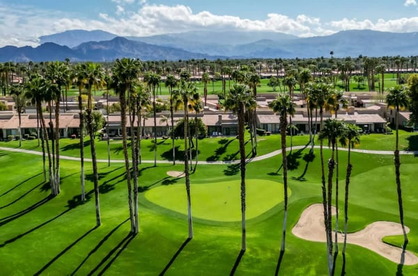 An aerial view of the resort showcases manicured golf greens, swaying palm trees, and the dramatic mountain backdrop surrounding the property.