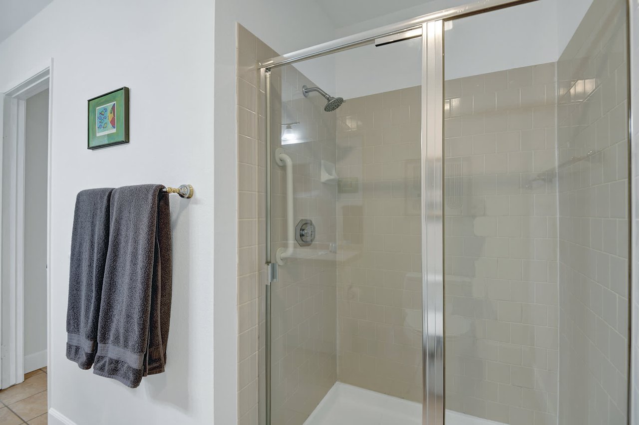 Step into your private spa-like retreat with a spacious walk-in shower featuring sleek glass doors and soothing neutral tile. Fresh towels await, ready for your refreshing morning start or relaxing evening wind-down.