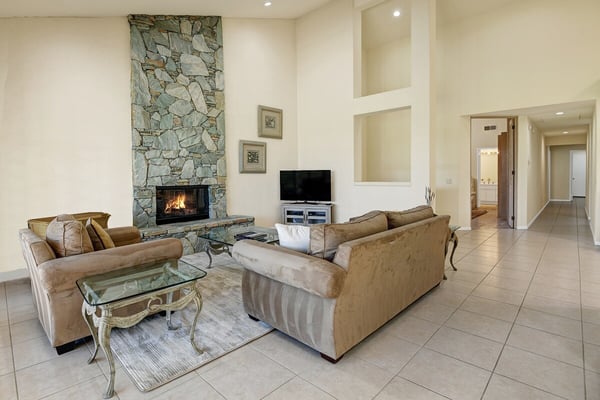 Sink into plush sofas beside a crackling stone fireplace in your spacious living area, where high ceilings and warm tile floors create an elegant yet cozy retreat.