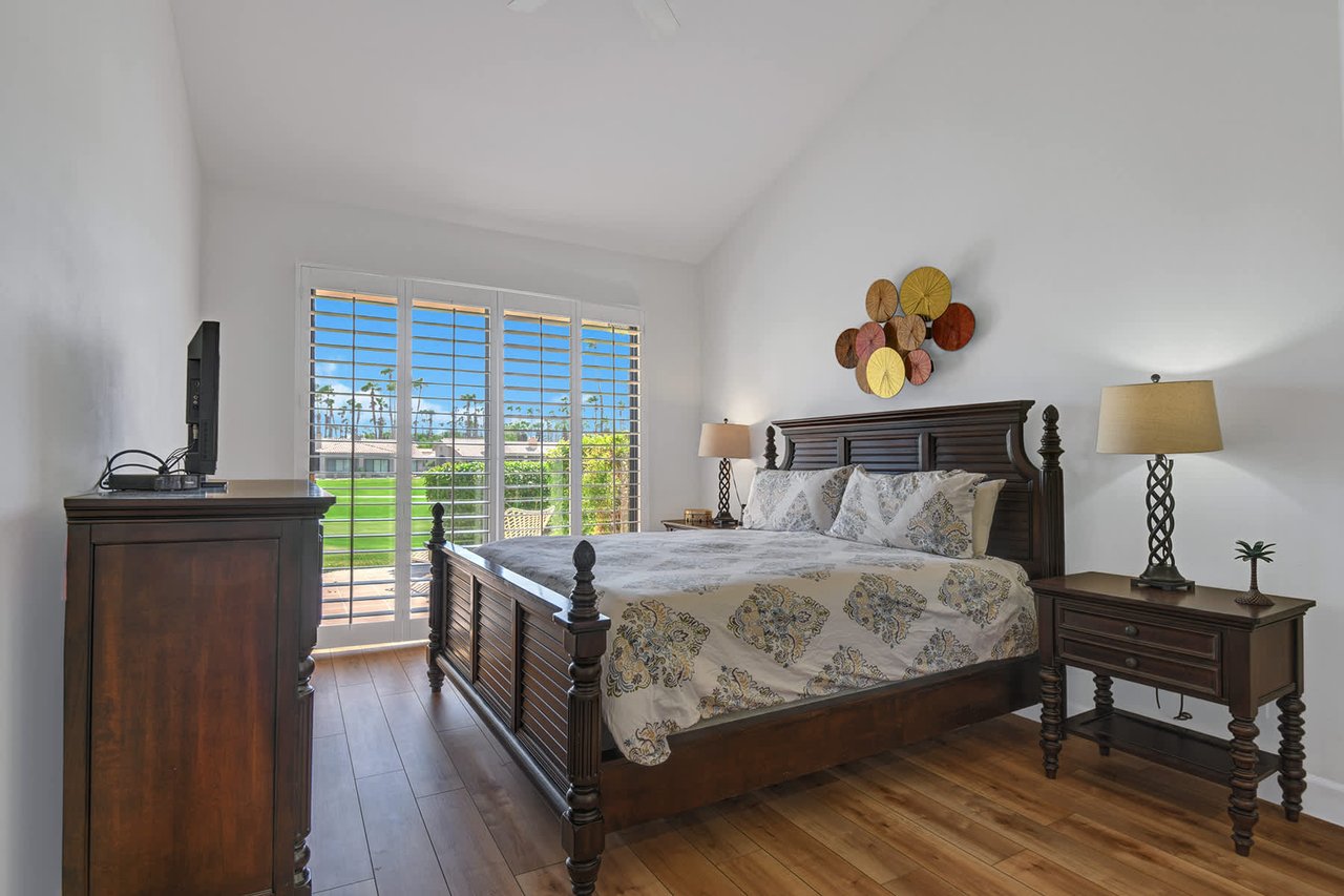 Unwind in your serene bedroom where natural light pours through plantation shutters, revealing lush greens just beyond. Rest easy in a classic four-poster bed with thoughtful bedside touches for your comfort.