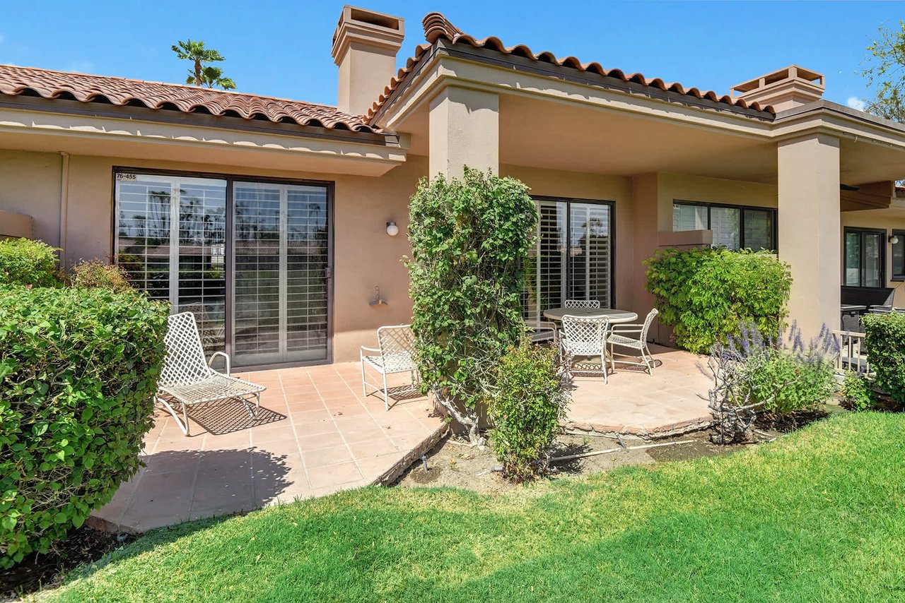This Mediterranean-style villa features a tiled patio with shaded seating, perfect for relaxing outdoors surrounded by lush greenery and blue skies.