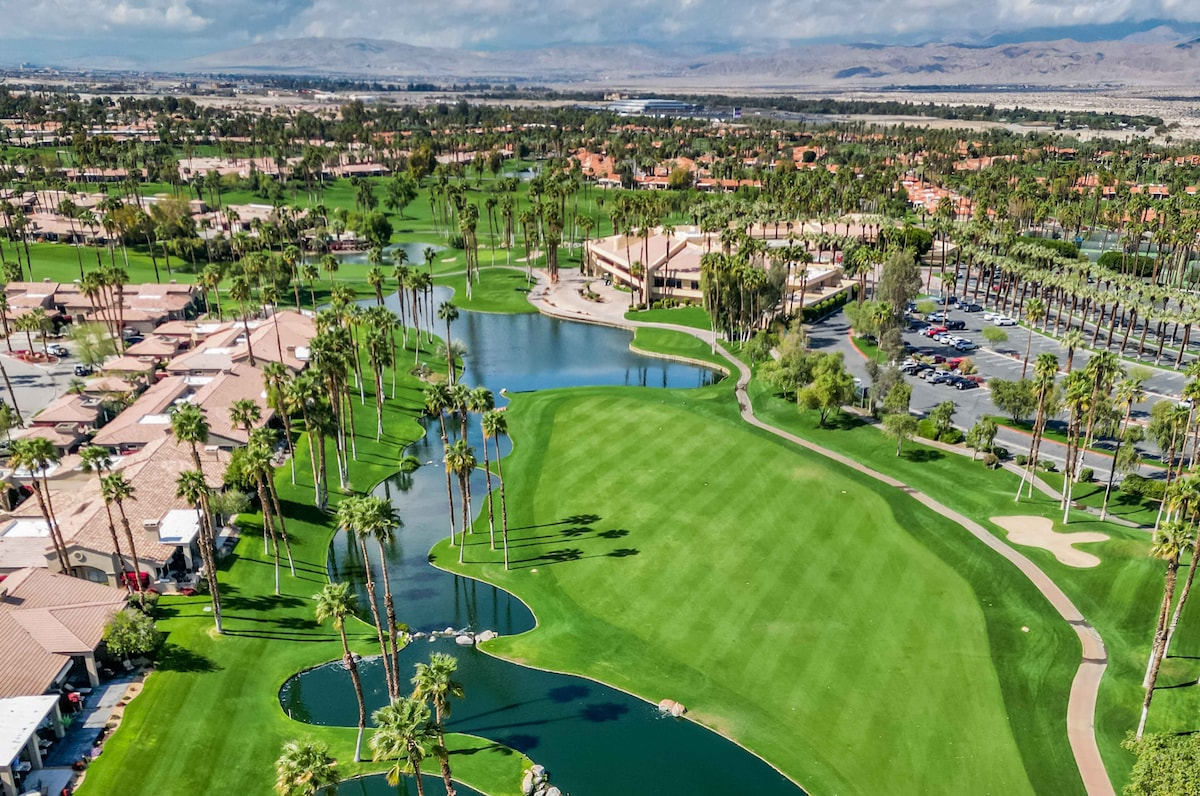 Aerial view of the resort nestled within a lush golf course community, framed by rolling desert mountains and sparkling water features.