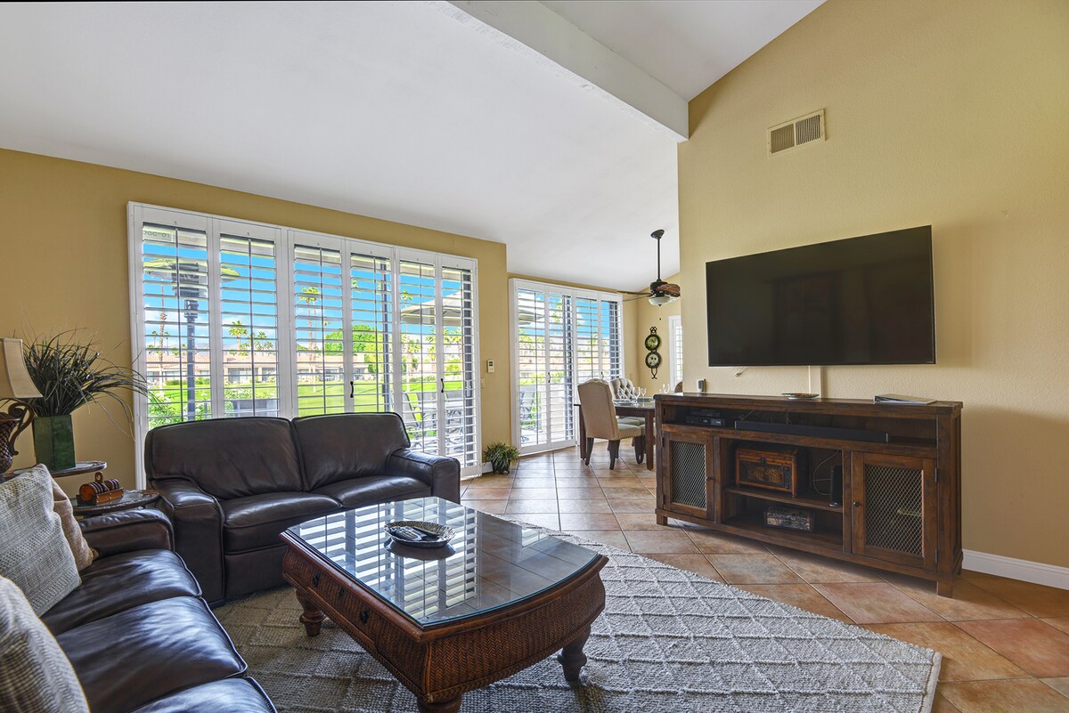 Sink into the plush leather sofas and unwind in your bright, spacious living room with vaulted ceilings and plantation shutters that frame views of lush greenery just beyond.
