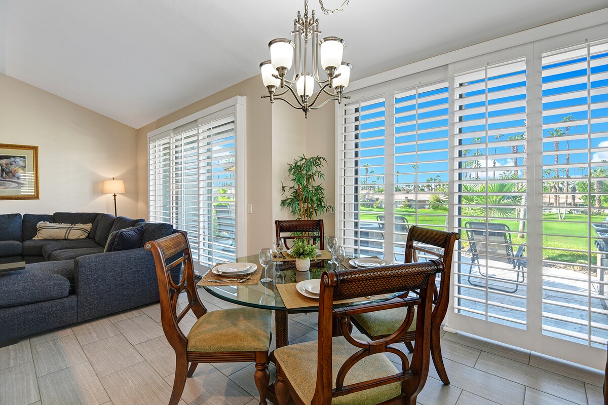 Unwind in your open living space where soft natural light filters through shutters and every window frames lush greens and palm trees just beyond your private patio.