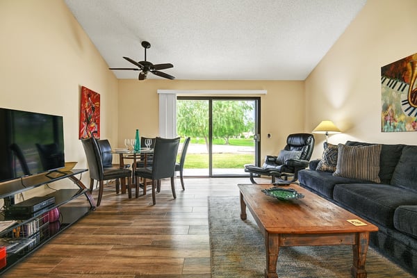Unwind in your open-concept living area where large sliding doors frame lush green views and warm natural light fills the space. Sink into the plush sofa and enjoy comfortable gatherings at the dining table.