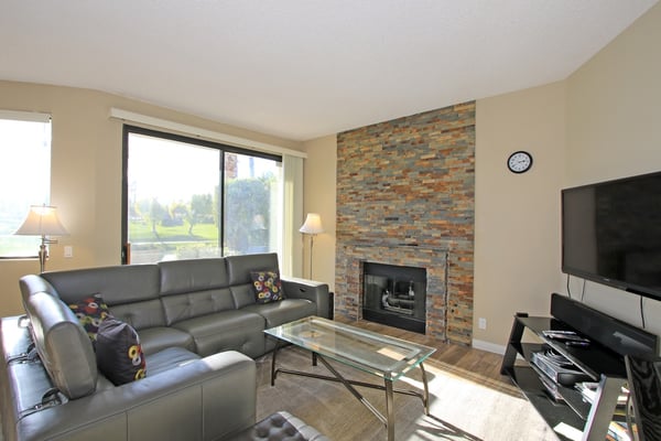 Unwind in your inviting living room, where a stunning stacked stone fireplace adds warmth and character. Sink into the comfortable sectional, enjoy the large flat-screen TV, and take in views of lush greenery through expansive windows.