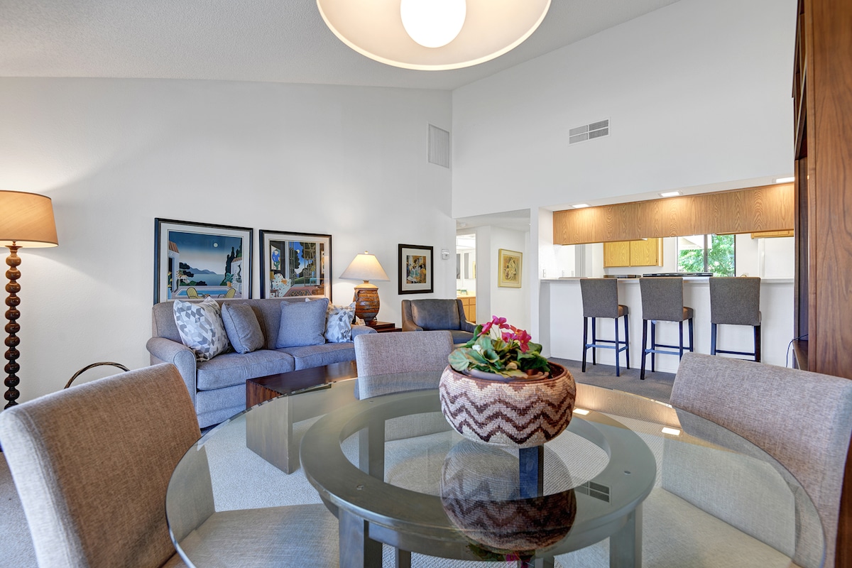 Settle into your bright, open-concept living space where coastal artwork and soft natural light create an instantly calming atmosphere. Gather around the glass dining table or unwind on plush seating—your home base for memorable vacation moments.