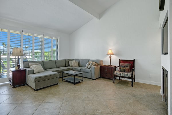 Settle into your spacious living room, where vaulted ceilings create an airy feel and large plantation shutters frame glimpses of swaying palms outside.