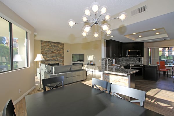 Bright, open-concept living space flows into a sleek kitchen with granite countertops and modern appliances. A stunning starburst chandelier adds elegance, while large windows flood the space with natural light.