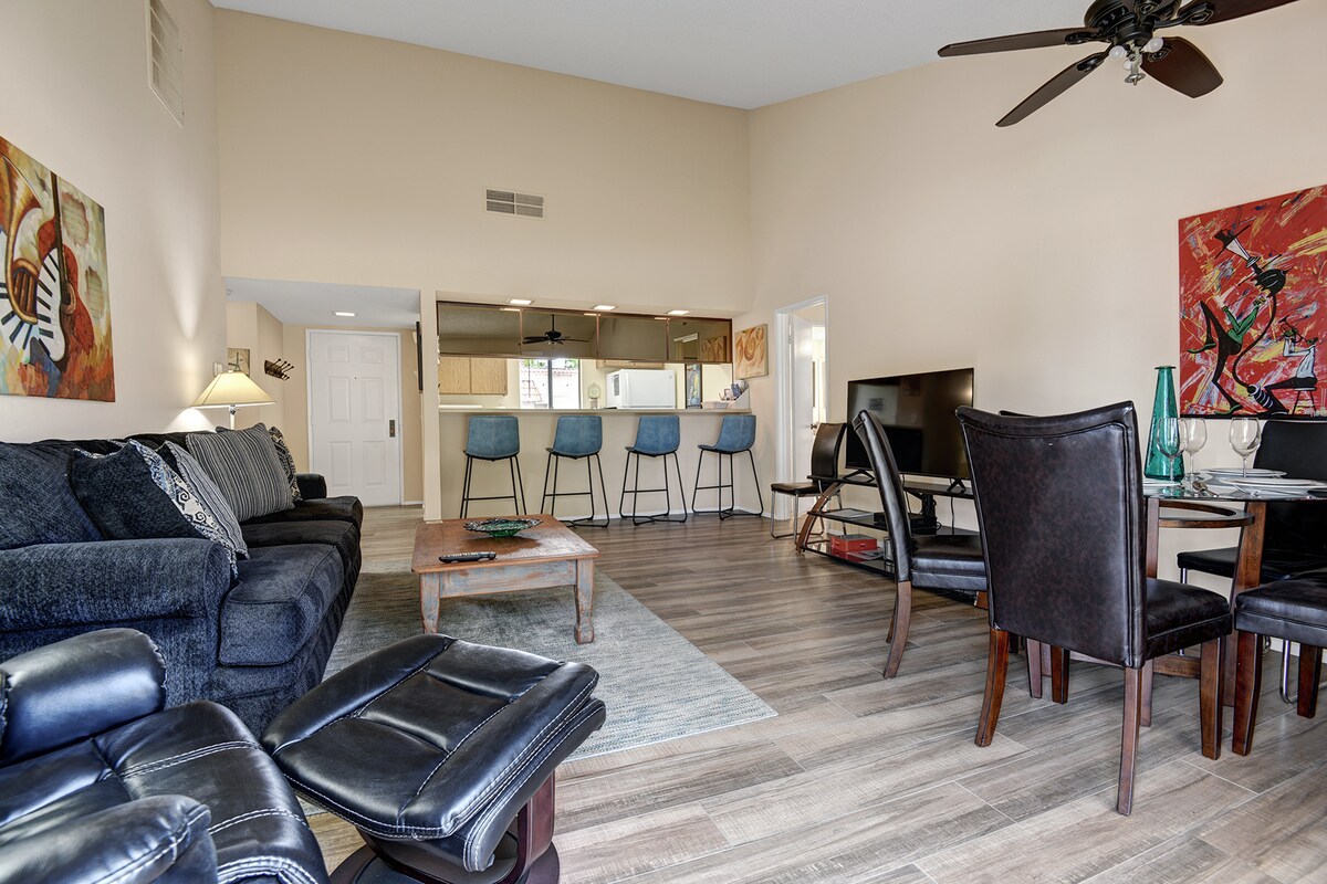 Step into your open-concept living space where comfort meets style. Plush seating invites you to relax, while the bright kitchen awaits your culinary adventures. High ceilings and colorful art create a warm, welcoming atmosphere.