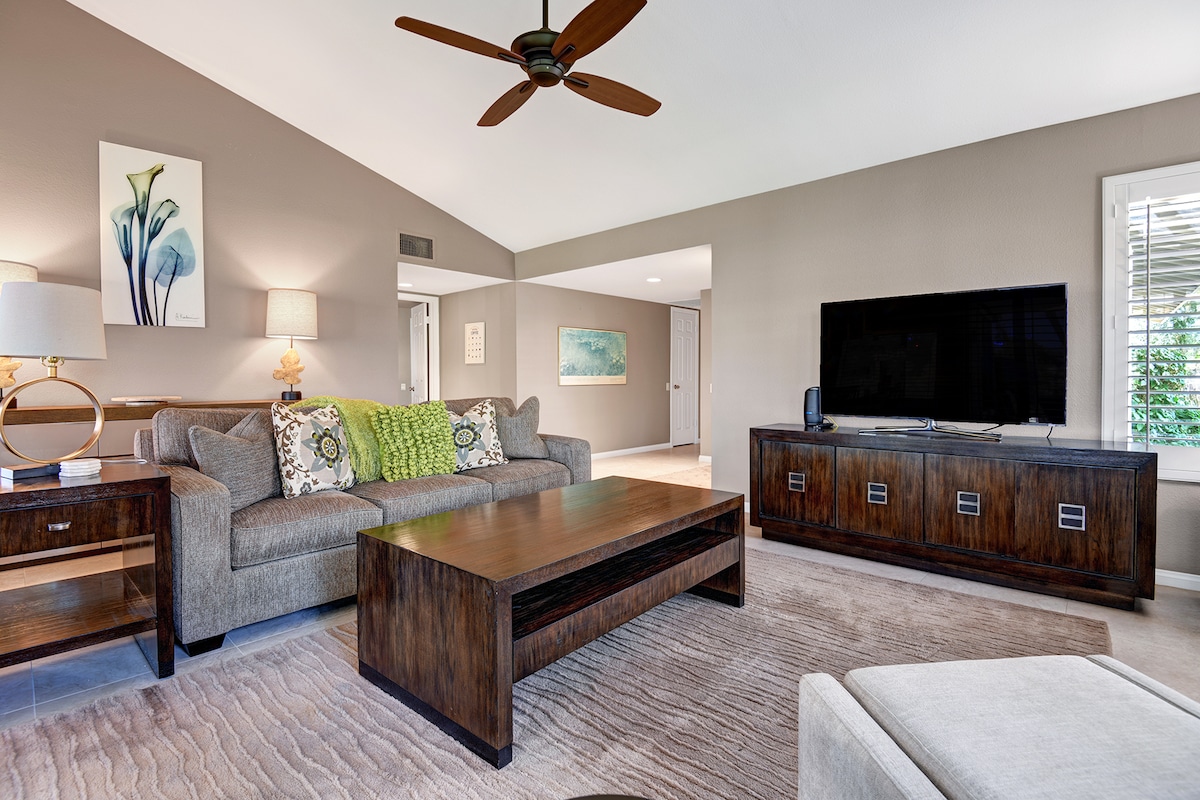 Unwind in this bright, welcoming living room with soaring vaulted ceilings and rich wood furnishings. Plush sofa seating, natural light, and a gentle ceiling fan create the perfect space to relax.