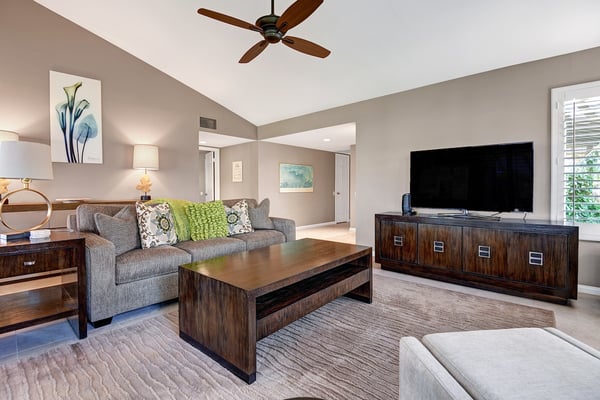 Unwind in this bright, welcoming living room with soaring vaulted ceilings and rich wood furnishings. Plush sofa seating, natural light, and a gentle ceiling fan create the perfect space to relax.