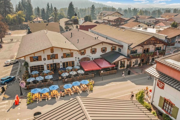 An aerial view capturing the charming alpine-style village architecture surrounded by forested mountains, showcasing the nearby dining and shopping area where local culture meets natural beauty.
