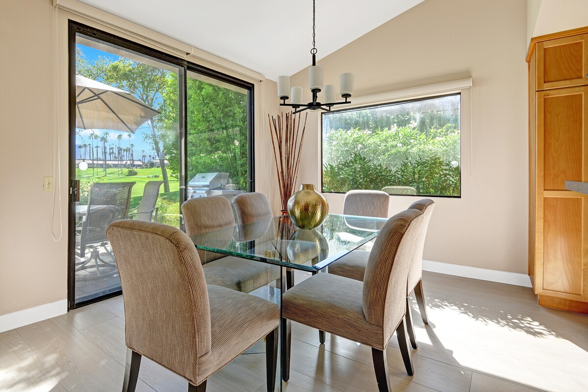 Natural light pours through floor-to-ceiling windows, framing your elegant dining space where outdoor garden views and patio access create a seamless indoor-outdoor flow for memorable meals.