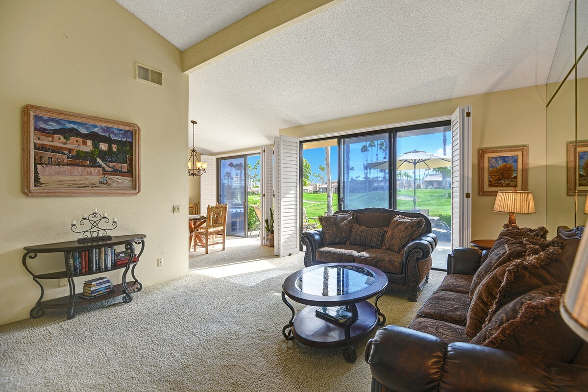 Step into your bright living room, where plush seating invites you to unwind. Open the glass doors to your private patio, and enjoy direct access to lush green lawns and sunny skies beyond.