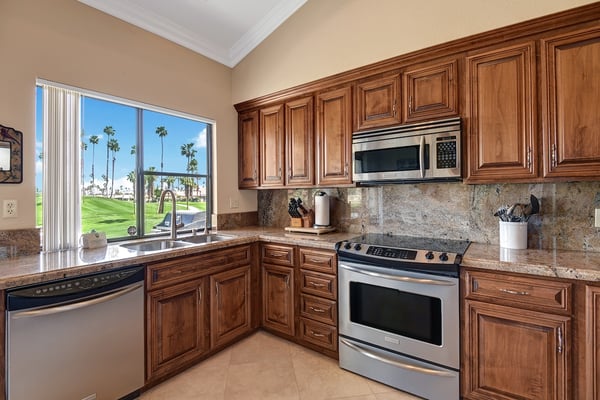 Cook with ease in your fully equipped kitchen, where warm wood cabinetry and granite counters set the scene for memorable meals. The bright window frames swaying palm trees and lush golf greens just outside.