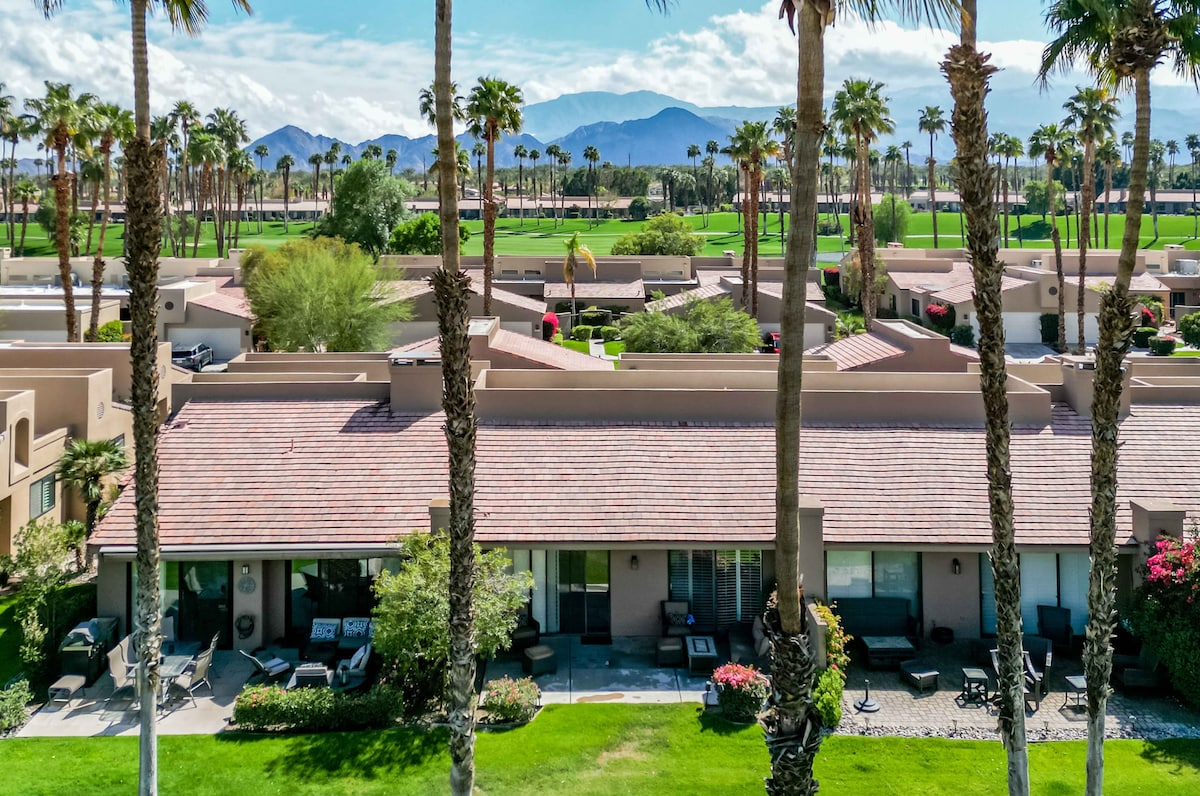 A stunning desert oasis showcasing the property's prime location, with majestic mountains framing the resort's lush green spaces, swaying palms, and nearby golf course. An ideal setting for relaxation and recreation.