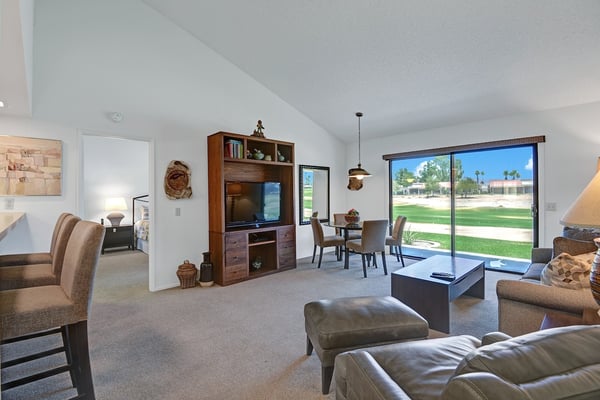 Relax in your light-filled living space with comfortable seating, a cozy dining area, and sliding glass doors opening to views of palm trees and green lawns.