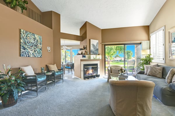 Unwind in your airy living room where soaring ceilings and a cozy fireplace meet abundant natural light streaming through large windows overlooking lush greenery.
